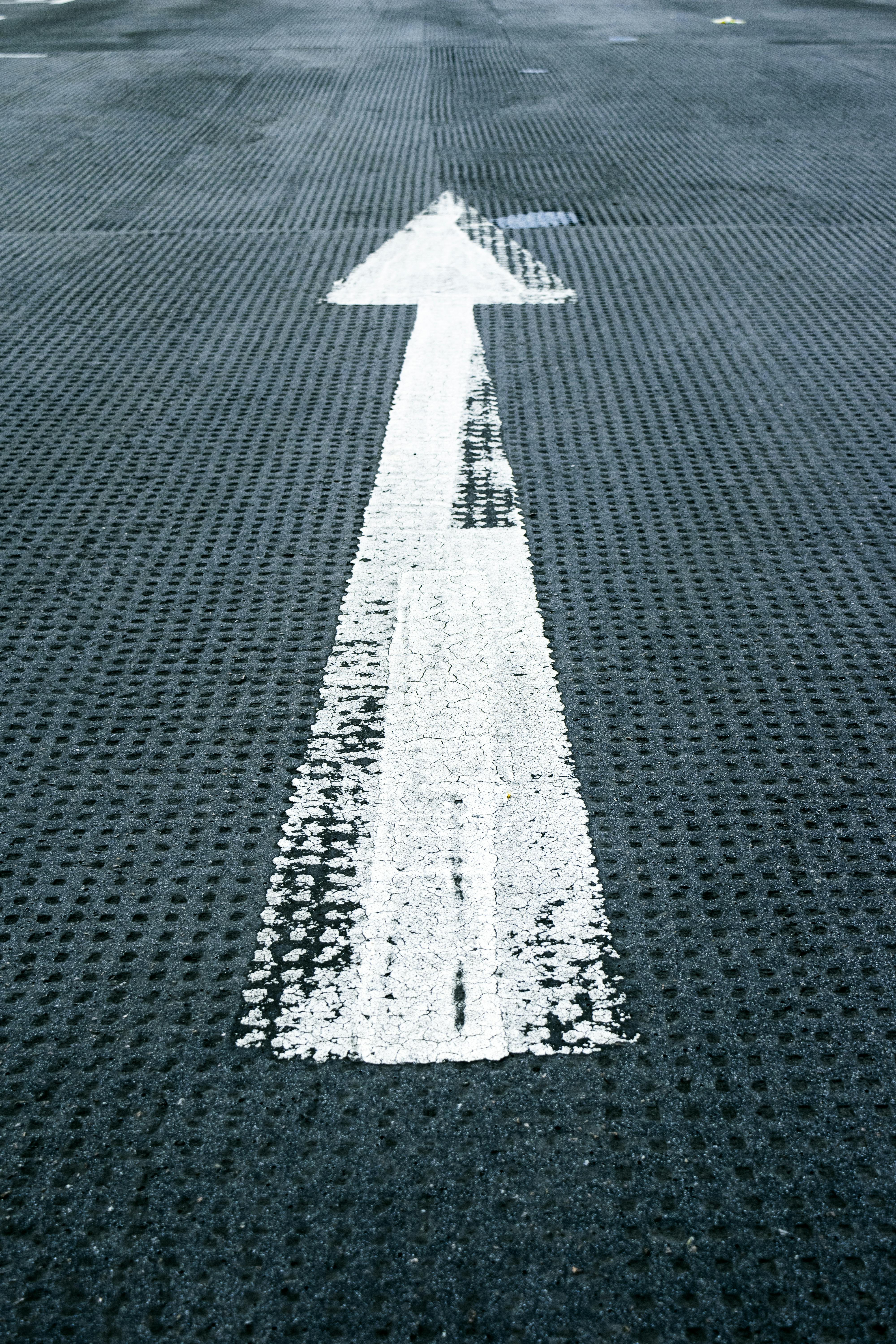 A white upward facing arrow on a paved road.